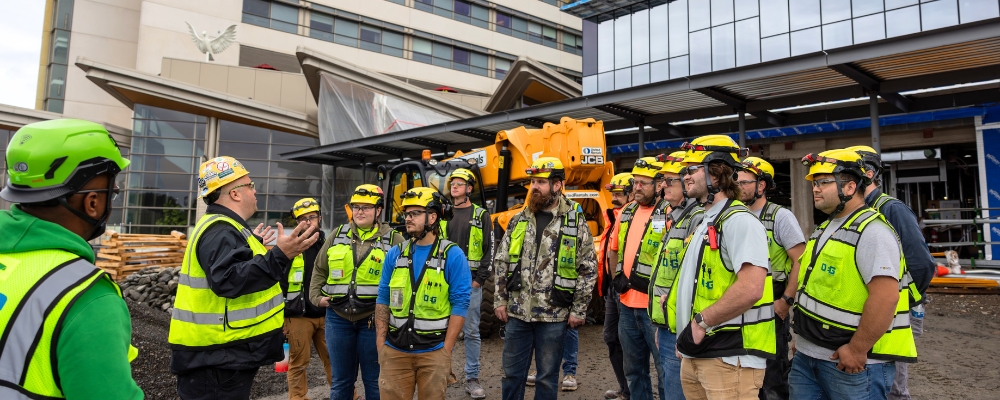 A group of electricians stand outside a a building listening to a foreman.