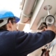 An electrician in a blue sweatshirt and blue helmet installs a building's security lighting.