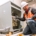 Male electrician in white hard hat and orange safety vest works on a commercial business's electrical system.