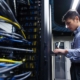 Man in blue shirt and black pants works in a data center on a computer.