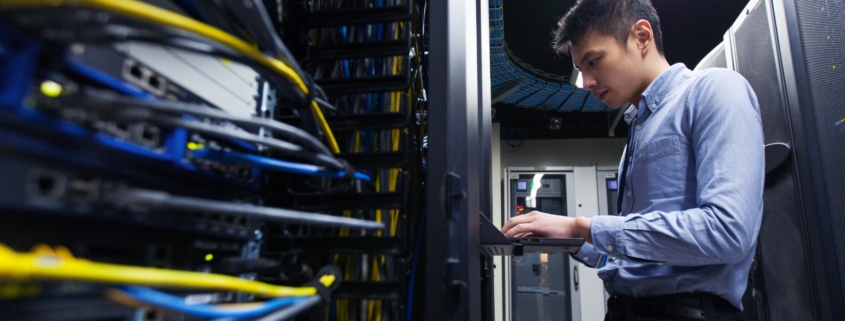Man in blue shirt and black pants works in a data center on a computer.