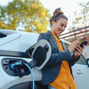 Woman sends messages on her smartphone while her electric vehicle is charging.