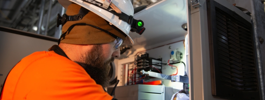 Electrical contractor in safety gear performs maintenance on a commercial electrical system.