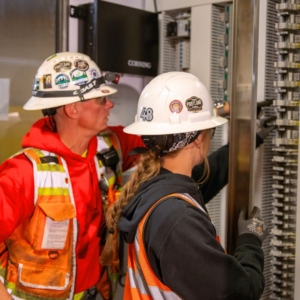 Two electricians fix the wiring of an electrical panel in a commercial building.