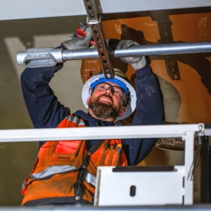 Commercial electrician adjusts electrical work in the ceiling of an industrial building.