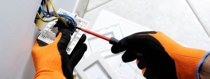 Electrician wears safety gloves while fixing a home electrical socket.