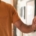 Man with beard wearing an orange t-shirt adjusts his smart thermostat to 74 degrees.
