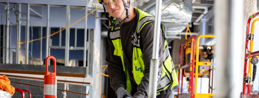 Industrial electrical contractor wearing a yellow hard hat and safety glasses, installing conduit in a building under construction.