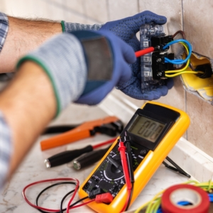 Electrician with blue safety gloves tests a home electrical circuit.
