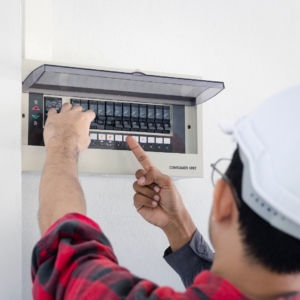 Residential electrician in red and black flannel shirt fixing a home electrical panel.
