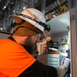 Electrician in orange t-shirt updates wiring in industrial facility.