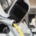 Close-up of an electric vehicle charging port with a yellow cable plugged in, with a person blurred in the background.