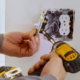 An electrician using a power tool on a light switch.